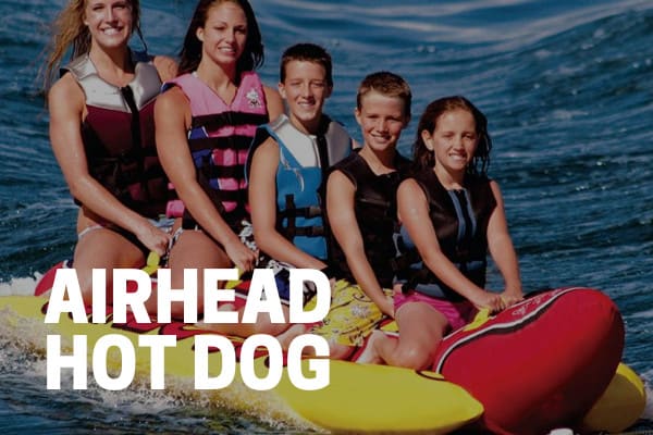 kids and adults riding on an airhead hot dog towable tube